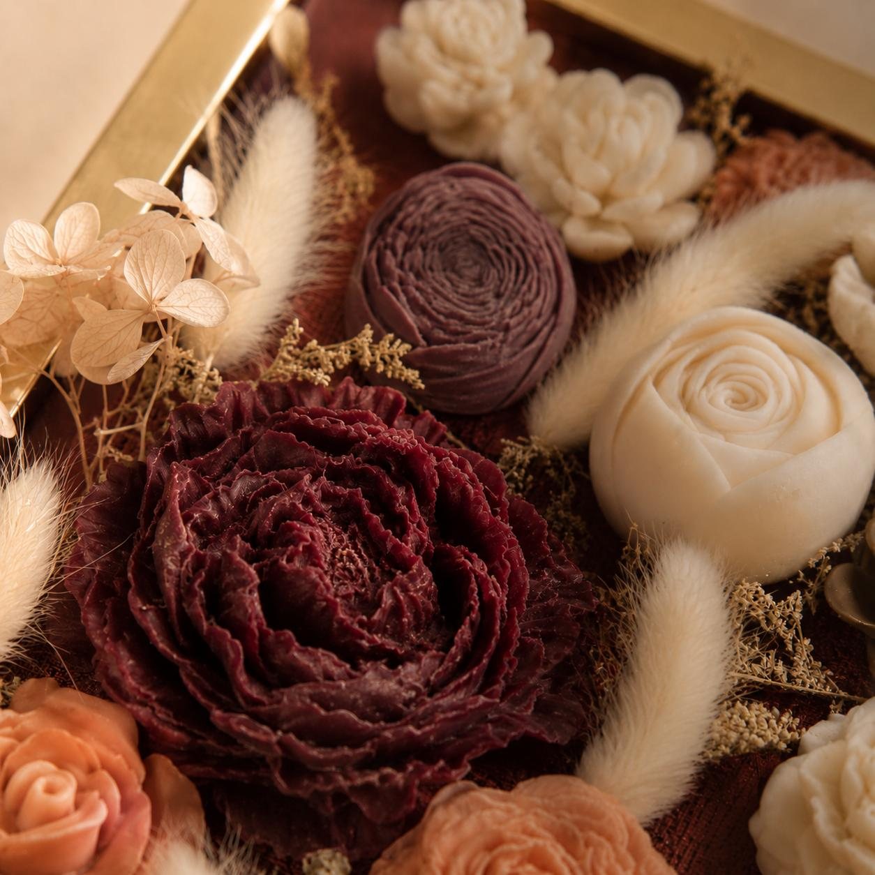 Gros plan d'un tableau : pivoine de cire bordeaux, roses crème et brins séchés
